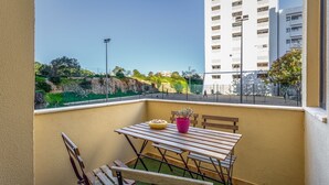 Un balcon avec une table et des chaises en bois, une plante en pot et une vue sur une rue où l’on peut voir des gens qui se promènent.
