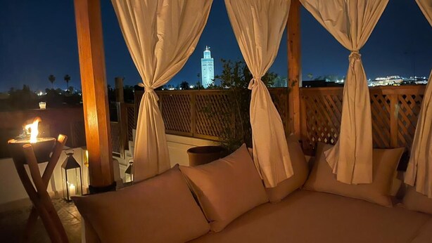 Ein gemütlicher Sitzbereich im Freien mit gepolsterten Bänken und einem Tisch mit Kerze, vor einer Skyline der Stadt bei Nacht.