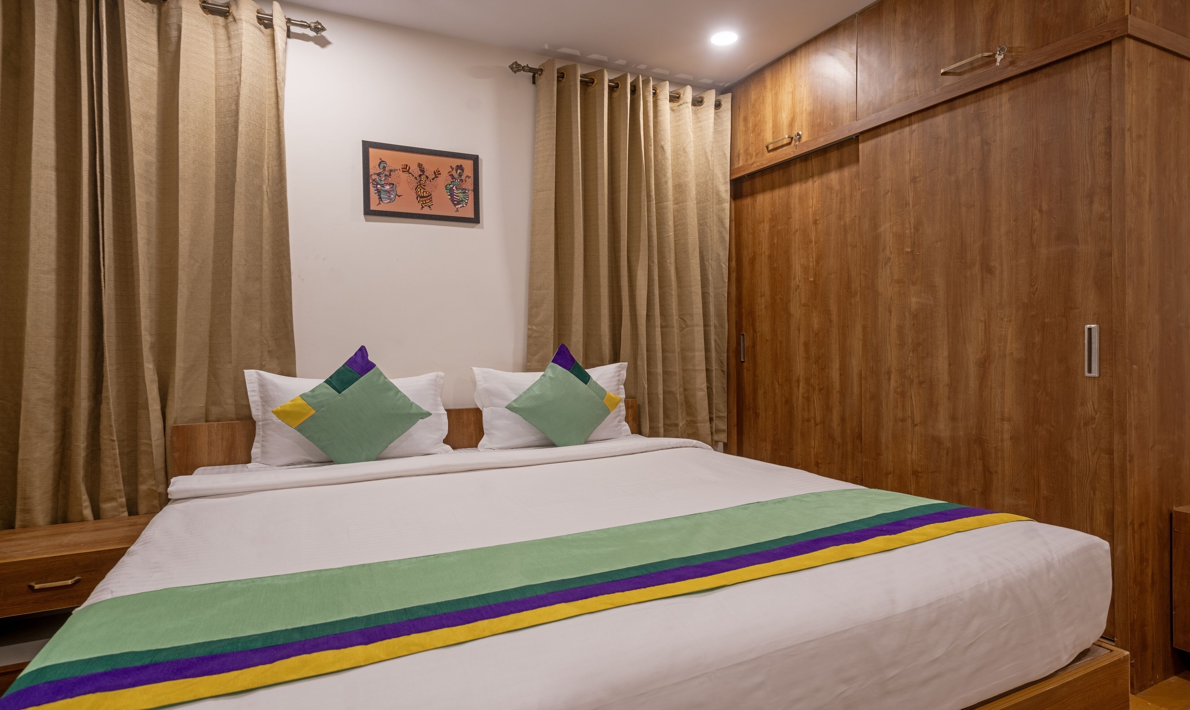 Habitación de hotel con cama, armario de madera, cortinas color crema y un cuadro en la pared.