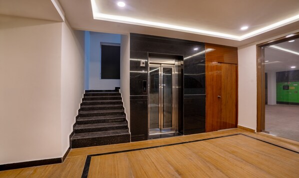 A modern elevator with a glass door, a wooden door, and a marble wall. - Treebo Purva Crest, Gachibowli DLF (Hyderabad)