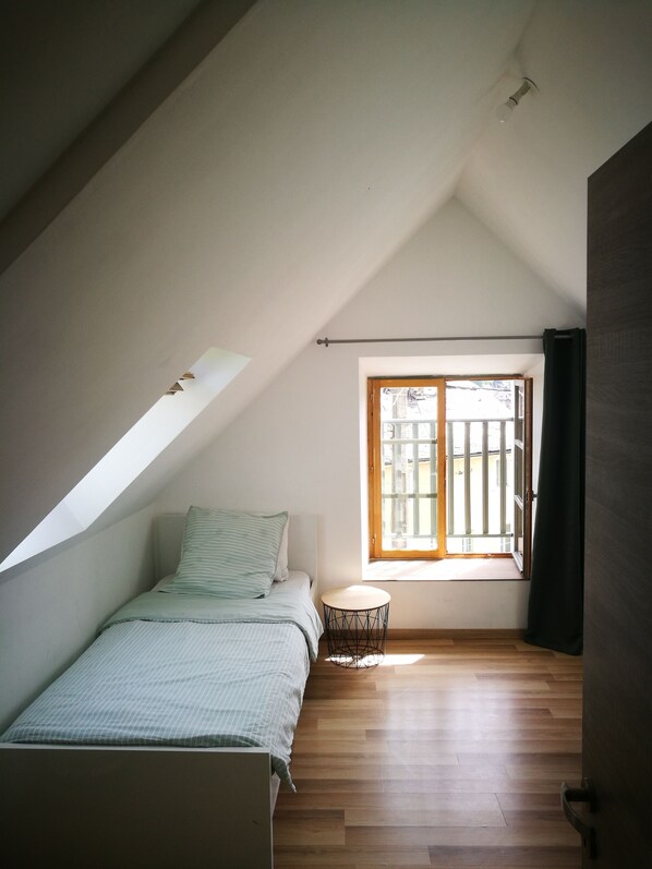 Un dormitorio con techo inclinado, una cama, una mesita redonda y un ventanal con vistas al exterior.