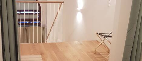 Un dormitorio con suelo de madera, una cama con sábanas blancas, un sillón colgante y una escalera que sube a un nivel superior.