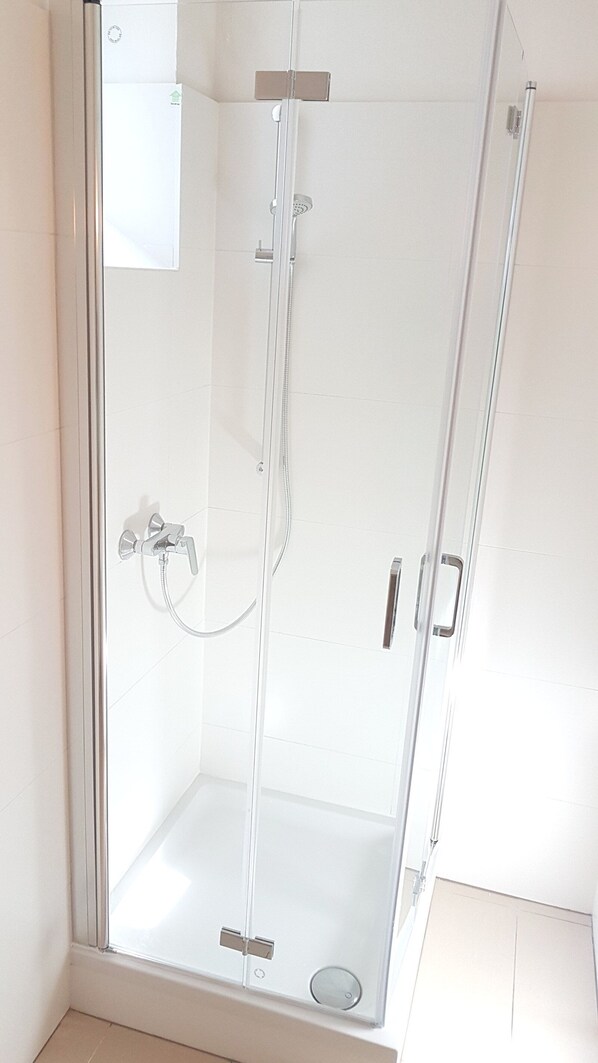 A glass-enclosed shower stall with a handheld showerhead and a wall-mounted faucet. - Sobieski City Center Apartments (Vienna)
