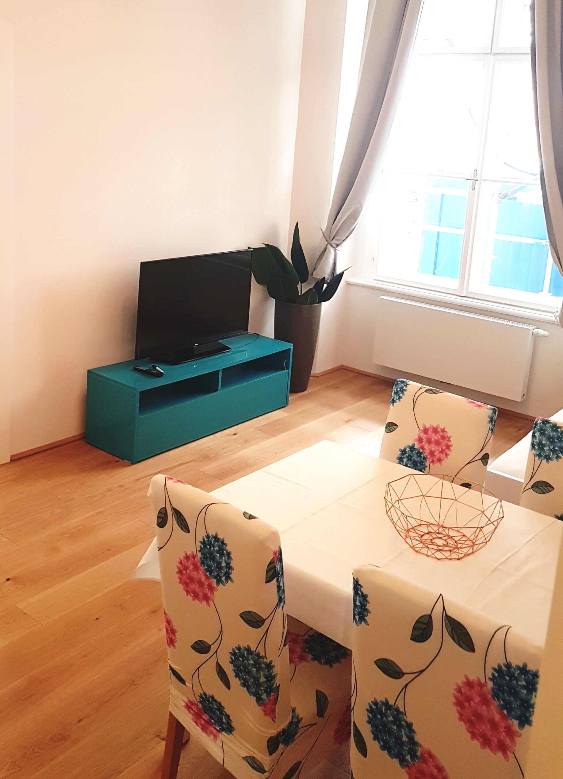 A dining area with a table and chairs, a teal storage unit, and a potted plant.