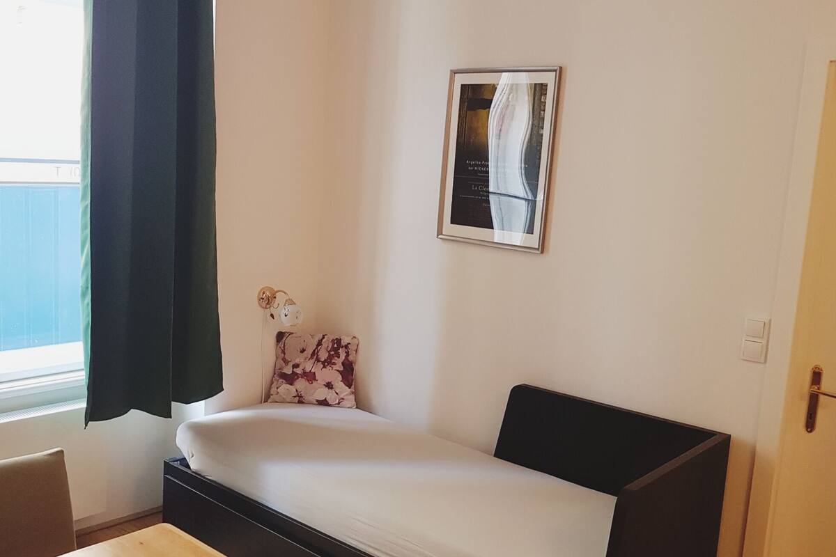 Una habitación pequeña y sencilla con una cama, una lámpara de pared y una puerta.