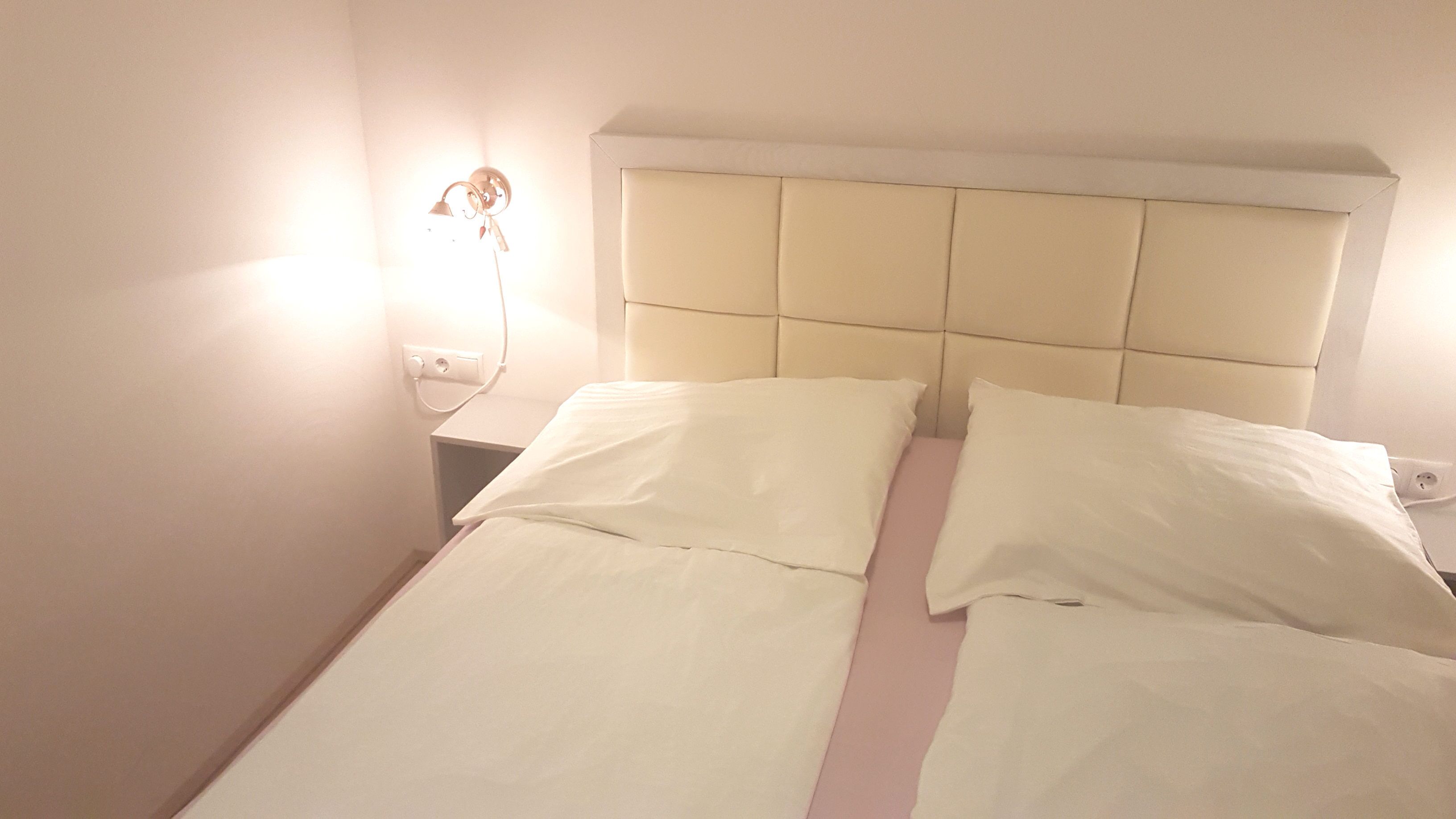 A single bed with a headboard, white bedding, and a bedside lamp.