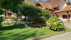 A traditional building with a tiled roof, surrounded by a well-maintained garden with various plants and flowers. - Hotel Pousada das Flores (Gramado)