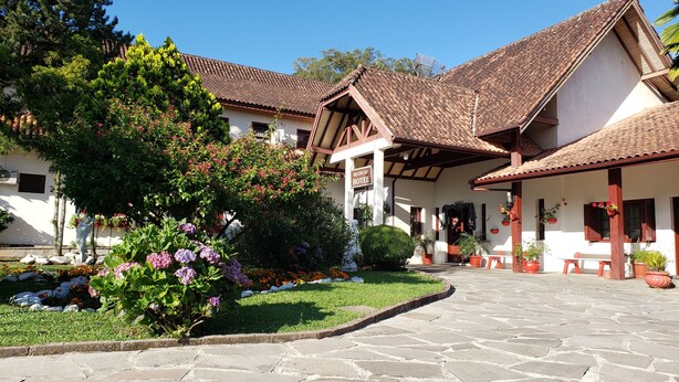 A traditional building with a tiled roof, a stone-paved courtyard, and potted plants. - Hotel Pousada das Flores (Gramado)