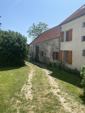 A rustic building with a dirt path leading to a stone entrance, surrounded by greenery.