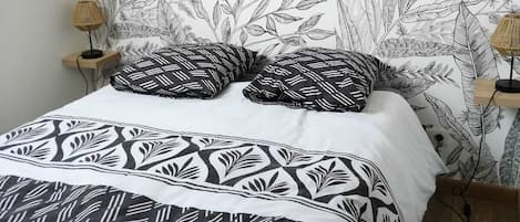 Un lit avec une couvre-lit à motifs et des oreillers, un mur recouvert d’un papier peint à motifs végétaux, et deux lampes de chevet.