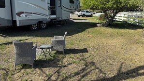 Una caravana con puerta corredera, una mesita pequeña y dos sillas de mimbre en un área cubierta de césped.