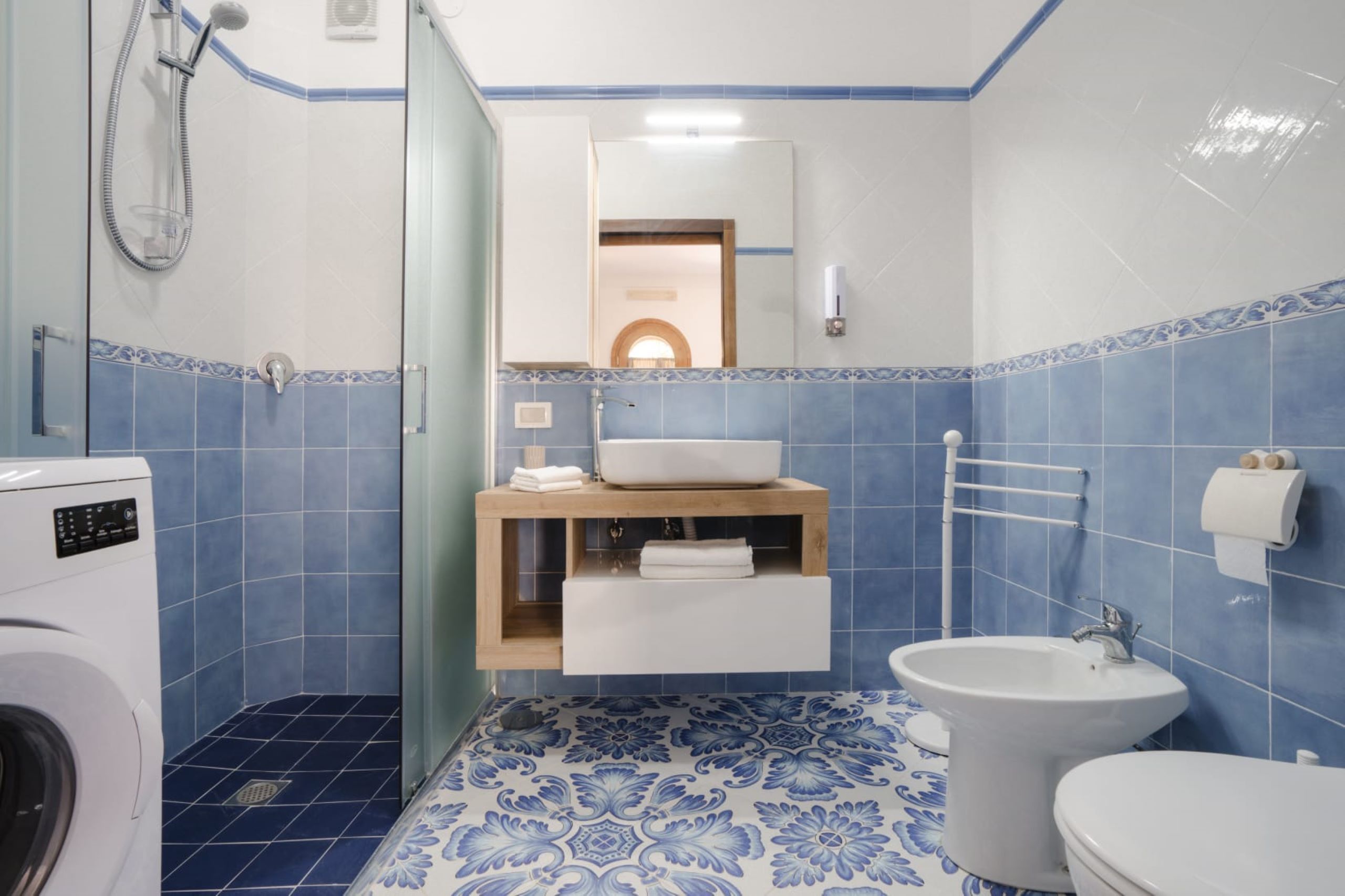 A bathroom with a washing machine, a sink, a bidet, and a mirror.