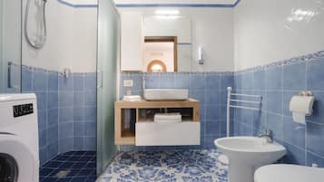 A bathroom with a washing machine, a sink, a bidet, and a mirror.