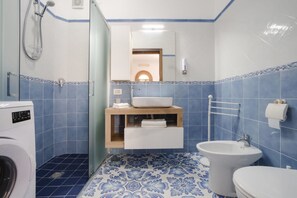 A bathroom with a washing machine, a sink, a bidet, and a mirror. - Villa Carrino 2 (Positano)