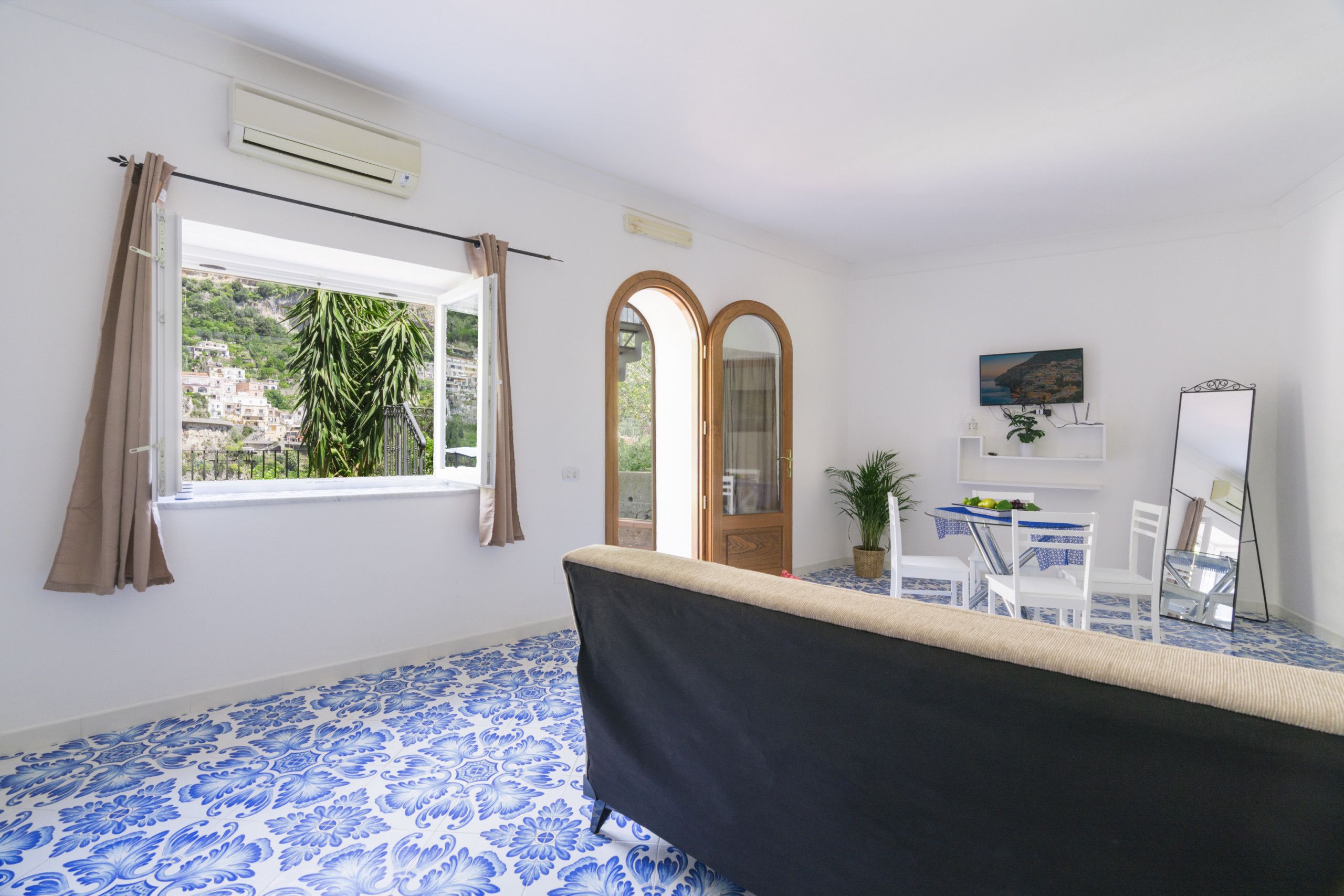A room with a large window, a bathtub, a dining table with chairs, and a mirror.