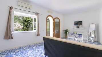 A room with a large window, a bathtub, a dining table with chairs, and a mirror.