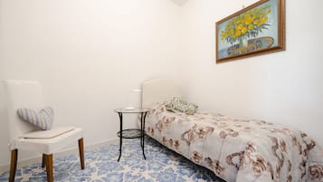 A small bedroom with a single bed, a chair, a small table, and a painting on the wall.