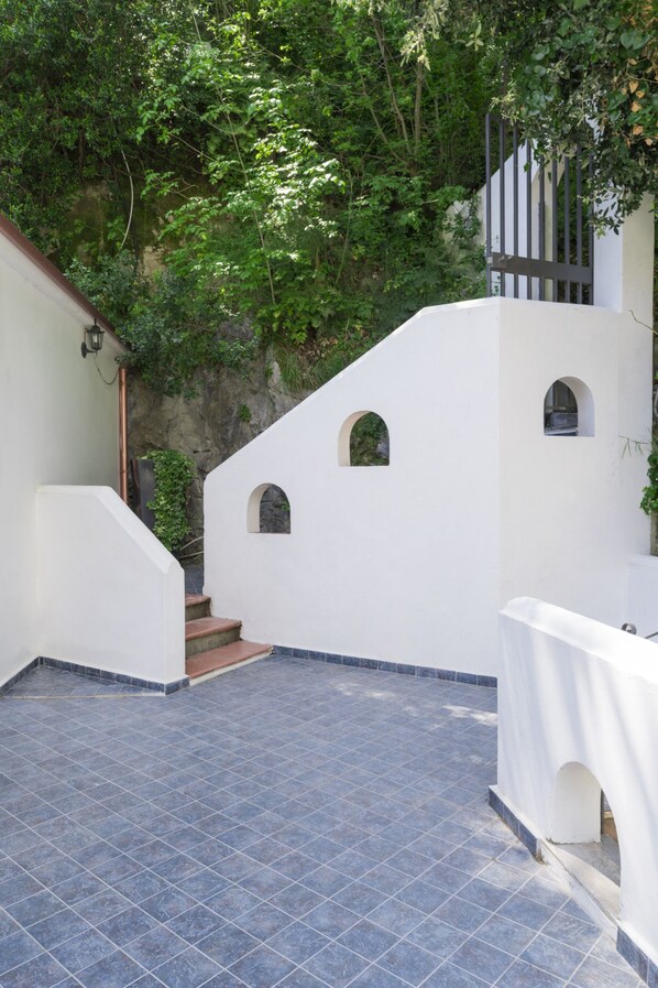 A white building with a tiled patio and a staircase leading to a door. - Villa Carrino 2 (Positano)