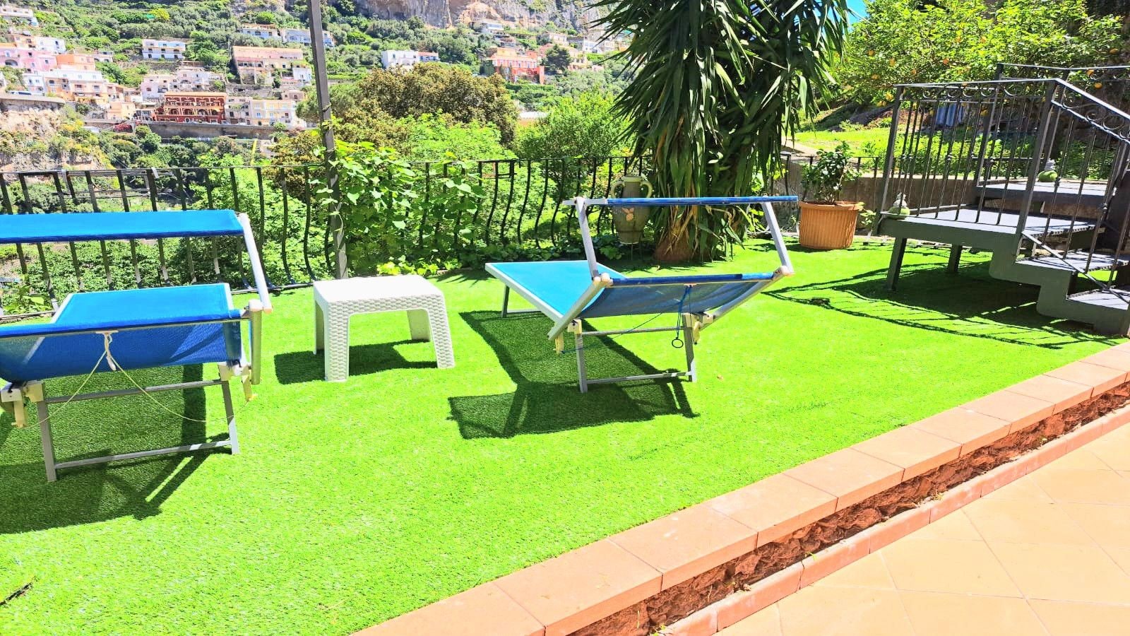 An outdoor seating area with a blue table and chairs, a white stool, and a metal bench.