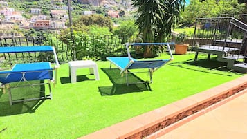 An outdoor seating area with a blue table and chairs, a white stool, and a metal bench.