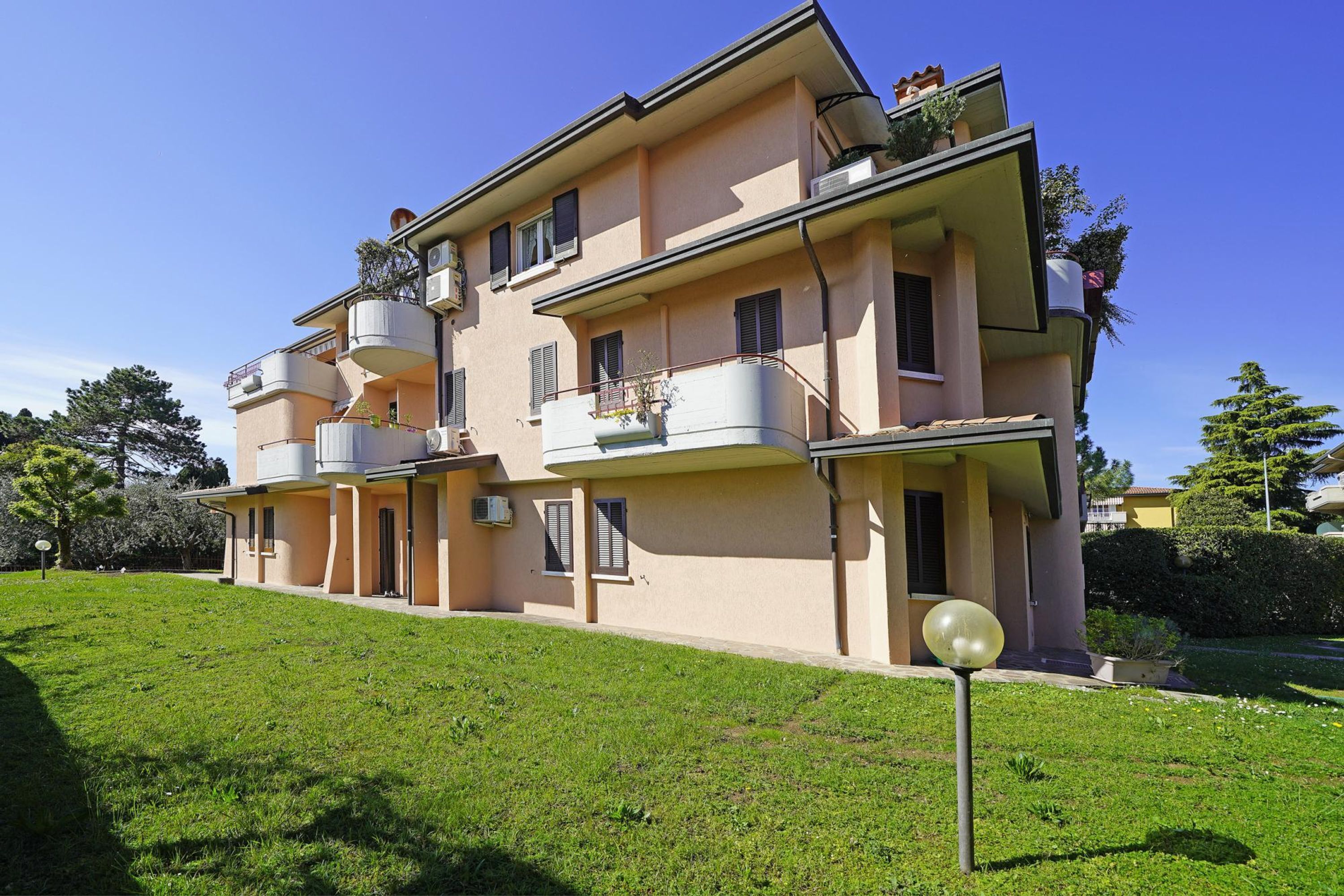 A multi-story residential building with balconies, a well-maintained lawn, and a clear sky.