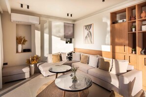 A modern living room with a sectional sofa, two round glass tables, a wooden cabinet, and a wall-mounted air conditioner. - Casa di Franco Seaview Heated Pool gym Hammam (Kissamos)