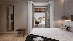 A modern bedroom with a large bed, a bedside table, a mirror, and a view of an outdoor patio.
