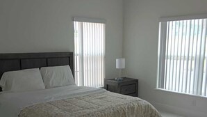 A bedroom with a bed, a nightstand, and two windows with blinds.
