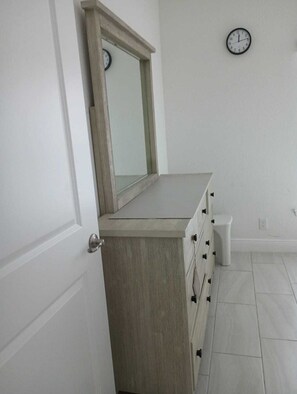 Un baño con tocador de madera, un espejo, un reloj en la pared y un cubo de basura.