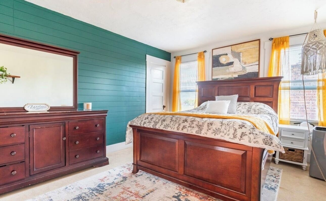 A bedroom with a wooden bed, a dresser, a nightstand, and a window with curtains.