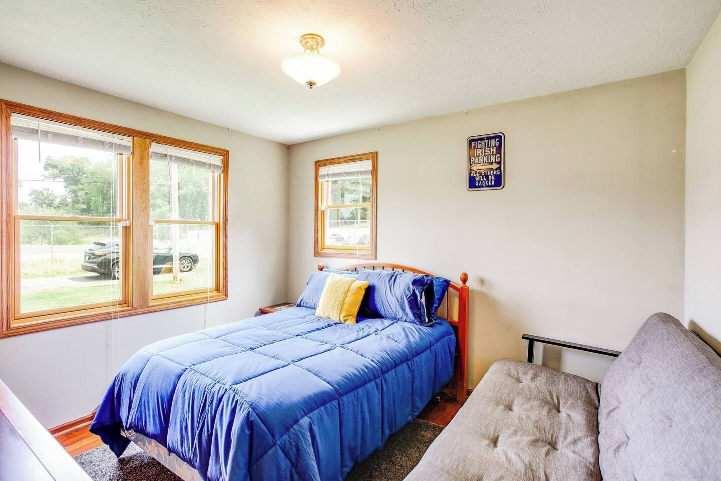 A bedroom with a bed, two windows, a ceiling light, and a sign on the wall.
