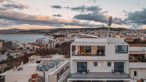A modern building with a rooftop terrace, a stadium in the background, and a coastal cityscape. - City Moments Penthouse I Close to Everything (Chania)