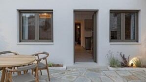 A modern house with a stone patio, wooden furniture, and a kitchen visible through an open door. - Lichnos Luxury Suites Stoa (Almyros)