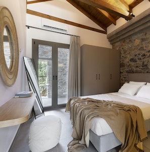 Ein Schlafzimmer mit Bett, Kleiderschrank, Schreibtisch mit Stuhl, Spiegel und Steinwand.
