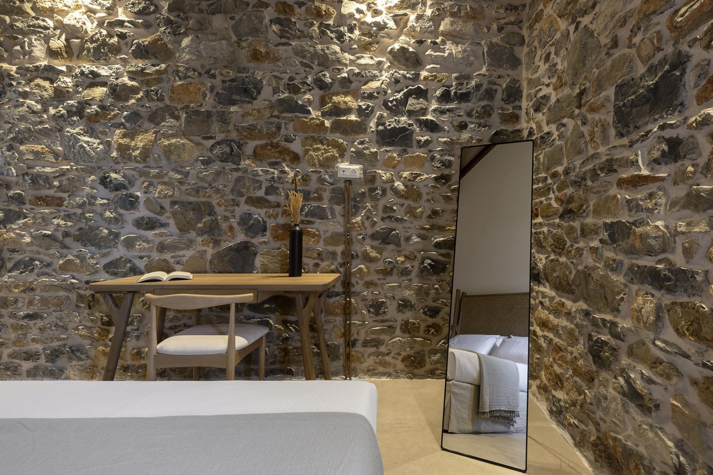 Une pièce avec un mur en pierre, un lit, un bureau avec une chaise et un miroir.