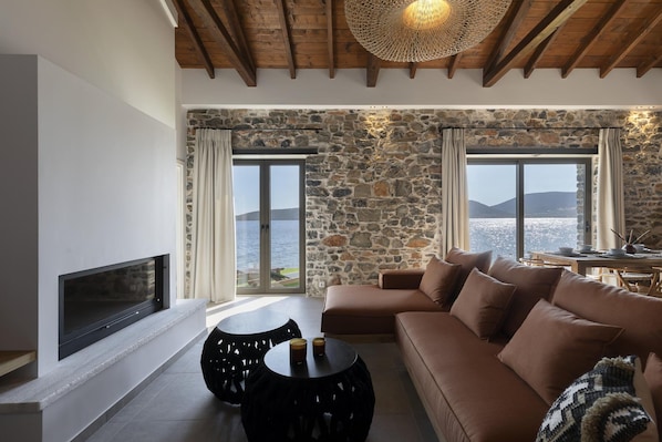 Un salon avec un mur en pierre, un canapé, une cheminée et une vue sur la mer.