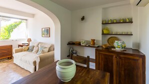 A cozy living room with a sofa, a dining table with a bowl, wooden cabinets, and shelves with decorative items. - Villa Delle Ninfeee by Napoliapartments (Anacapri)