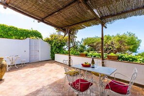 An outdoor patio with a table and chairs, a pergola, and a view of greenery and trees. - Villa Delle Ninfeee by Napoliapartments (Anacapri)