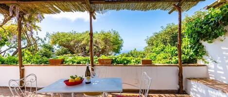 An outdoor patio with a table and chairs, a bottle of wine, and a basket of lemons.
