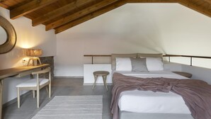 Une chambre avec un plafond en pente, un lit avec des oreillers, une table de chevet, une chaise et une lampe.