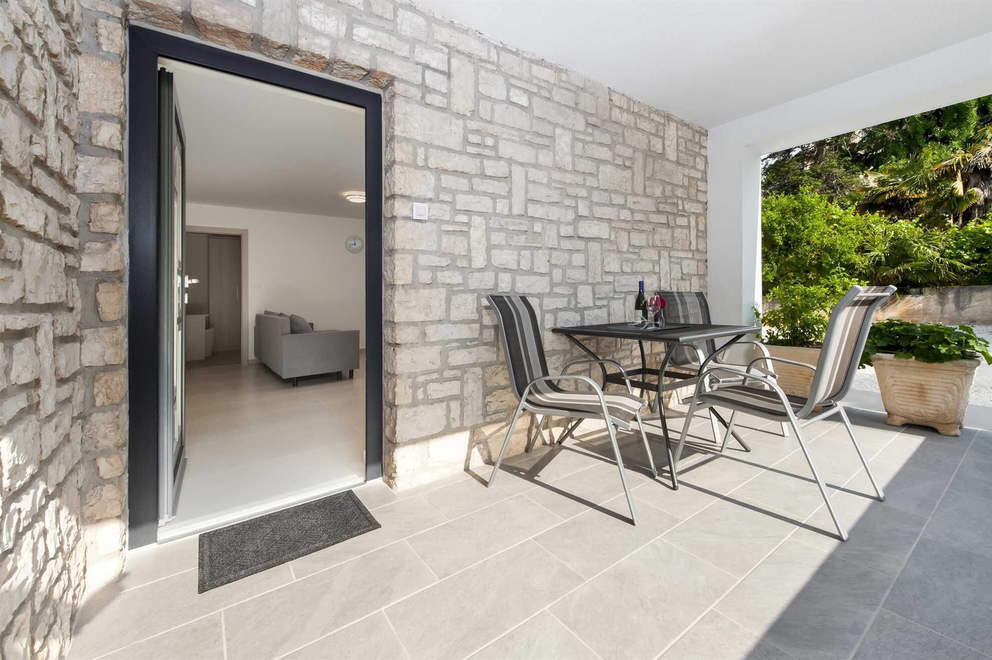 Un patio exterior con una pared de piedra, una mesa de comedor con sillas y una planta en maceta.