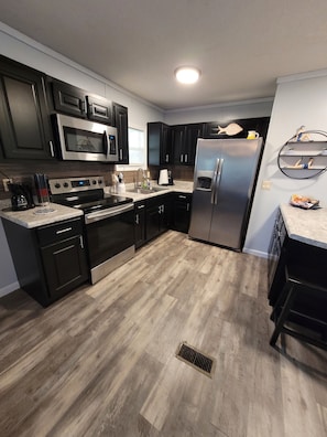 A modern kitchen with dark cabinetry, stainless steel appliances, and a light wood floor. - CROSSROADS TO PICKWICK THE PORCH  (Iuka)
