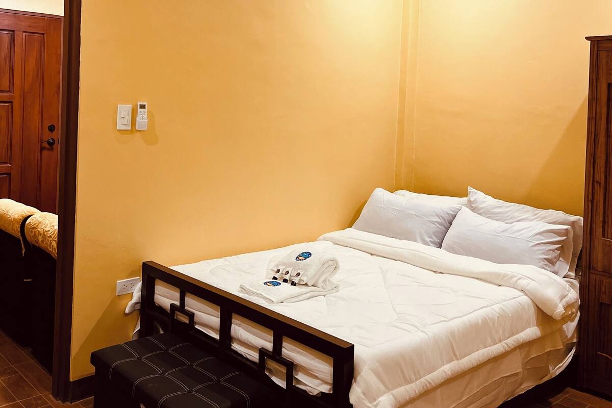 Ett hotellrum med en säng, en träbänk och en dörr.