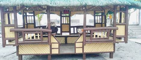 A thatched-roof gazebo with wooden benches and a sign prohibiting smoking.