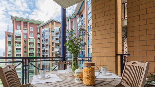 Ein Balkon mit einem Frühstückstisch, einer Blumenvase und einer Cornflakes-Glase.