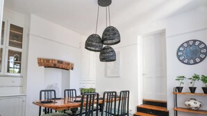A dining area with a wooden table and chairs, a black woven pendant light, a clock on the wall, and a staircase leading to another room. - 18 Ffordd Tanrallt (Prestatyn)