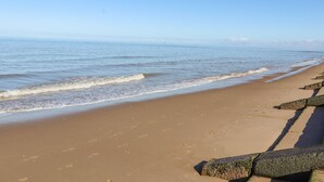 A sandy beach with waves, a clear sky, and a distant shoreline. - 18 Ffordd Tanrallt (Prestatyn)