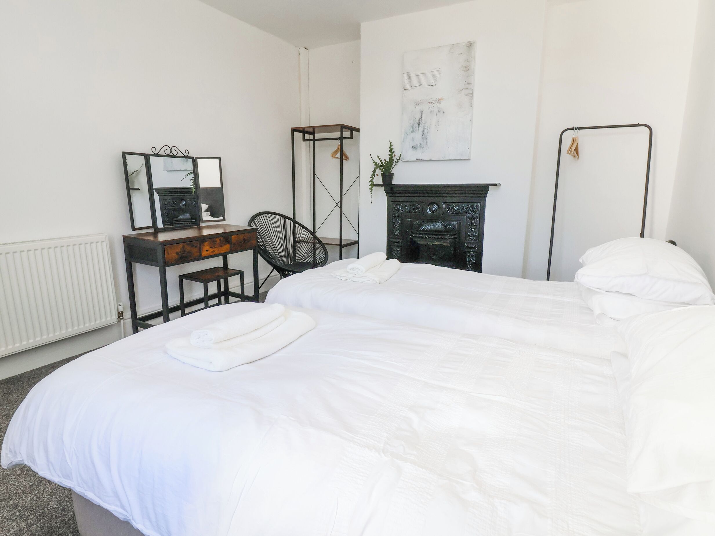 A bedroom with two beds, a dresser, a chair, a mirror, a fireplace, and a radiator.