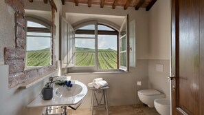 A bathroom with a large window, a sink, a toilet, and a door. - Le Colombelline 12 Emma Villas (Montepulciano)