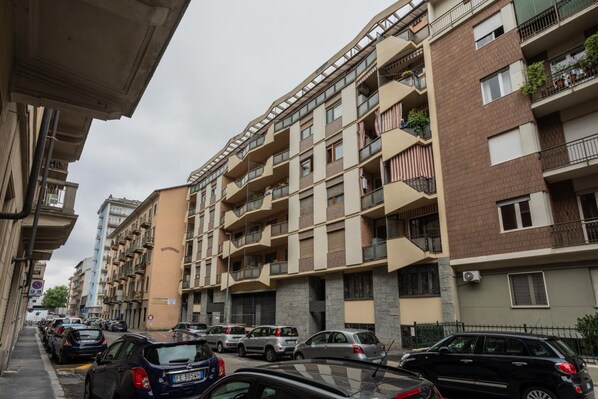 Un edificio residenziale a più piani con balconi, auto parcheggiate e cielo sereno.